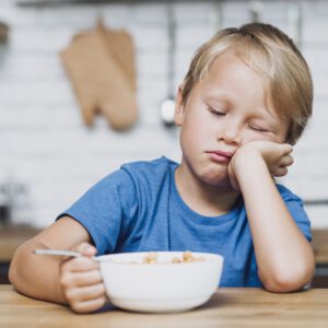 Test płatków śniadaniowych: chłopiec zniechęcony opiera głowę na dłoni nad miską płatków śniadaniowych