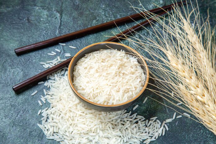 Arsen w ryżu: miska wypełniona ryżem na granatowym tle część ryżu wysypano na blat pałeczki i kłos zboża