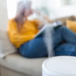 Test oczyszczaczy powietrza: Kobieta siedząca na kanapie i czytająca, a na pierwszym planie oczyszczacz powietrza z funkcją nawilżania