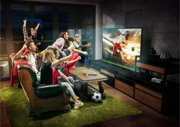 Test małych telewizorów: Grupa entuzjastycznie reagujących osób ogląda mecz w telewizji