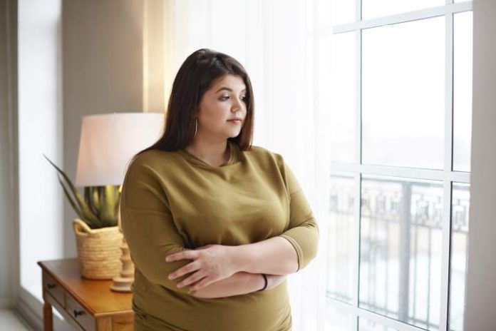 5 rzeczy, przez które nie możesz schudnąć: Kobieta z nadwagą patrzy przez okno