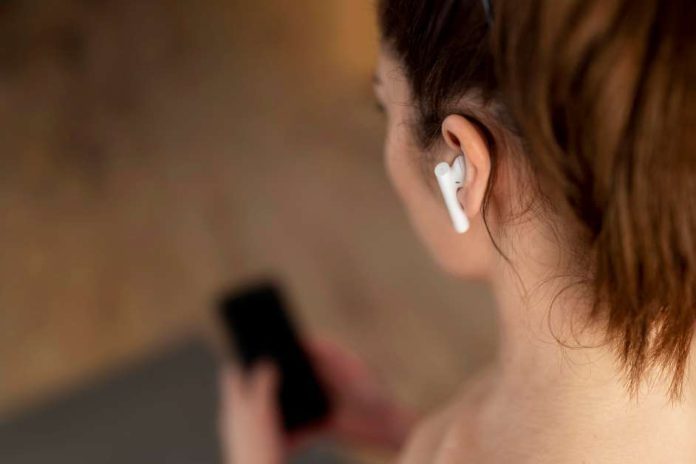 Jakie słuchawki douszne? Przybliżenie na kobietę widoczną od tyłu ze smartfonem w dłoni i słuchawkami w uszach